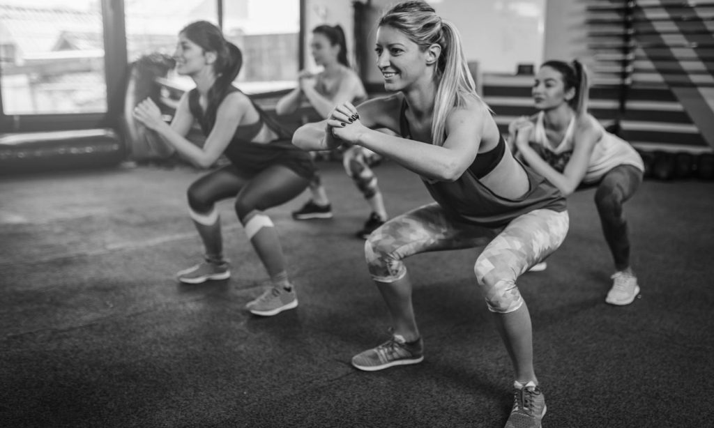 Groupe de femmes réalisant des squats pendant un cours d’abdos-fessiers