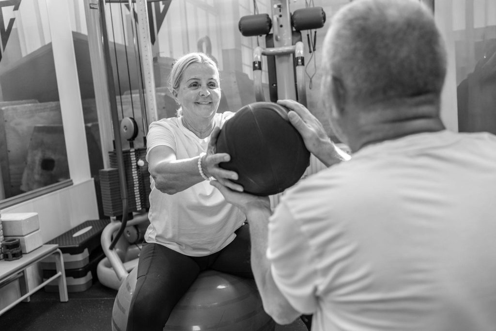 Coach accompagnant une femme senior pendant un exercice avec un medicine-ball