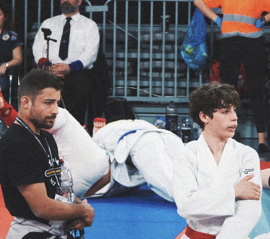 Entraîneur observant un jeune compétiteur de Jiu-jitsu Brésilien entre deux combats afin d’évaluer son état de récupération.