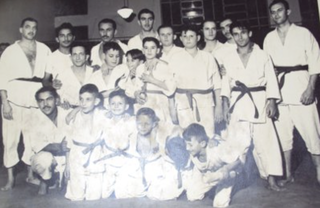 Photographie historique d’Octávio de Almeida entouré de ses élèves adultes et enfants en kimono dans son académie de jiu-jitsu à São Paulo, au Brésil, dans les années 1960.